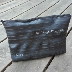 Könnte beinhalten: Schwarze Reißverschlusstasche aus recycelten Fahrrad-Schläuchen. Die Tasche trägt den Schriftzug "SCHWALBE".