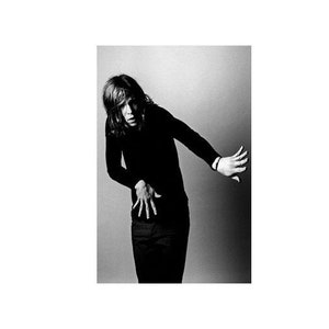 May include: A black and white photo of a person wearing a black long-sleeved shirt and black pants. The person is posing with their arms outstretched and their hands open.