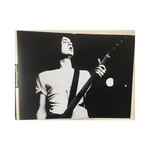 May include: Black and white photo of a person playing a bass guitar on stage. The person is wearing a white t-shirt and is looking up at the ceiling.