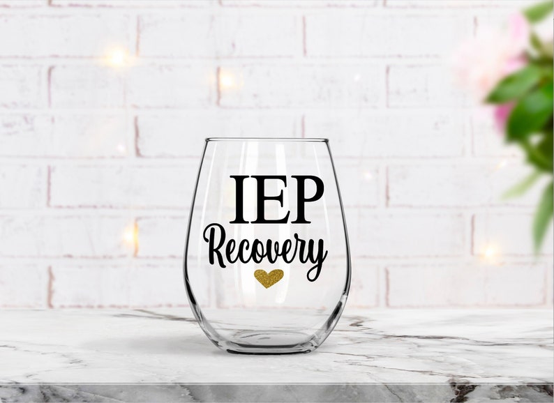 Pu&ograve; includere: Un bicchiere da vino in vetro trasparente con un adesivo in vinile nero che recita "IEP Recovery" con un cuore di glitter dorato.