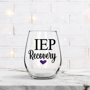 Pu&ograve; includere: Un bicchiere da vino in vetro trasparente con un adesivo in vinile nero che recita "IEP Recovery" con un piccolo cuore viola.