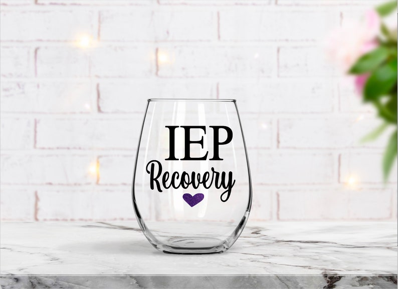 Pu&ograve; includere: Un bicchiere da vino in vetro trasparente con un adesivo in vinile nero che recita "IEP Recovery" con un piccolo cuore viola.
