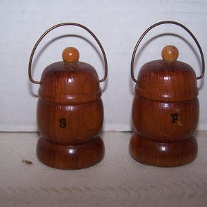 May include: A pair of vintage wooden salt and pepper shakers. Each shaker is barrel-shaped with a small wooden knob on top and a metal handle. The letter "S" is on one shaker and "P" on the other.