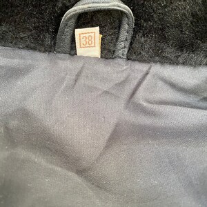 K&ouml;nnte beinhalten: Nahaufnahme des Futters einer schwarzen Lederjacke mit einem braunen Leder-Etikett, auf dem "38" in einem Quadrat steht.