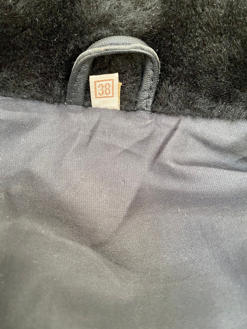 K&ouml;nnte beinhalten: Nahaufnahme des Futters einer schwarzen Lederjacke mit einem braunen Leder-Etikett, auf dem "38" in einem Quadrat steht.