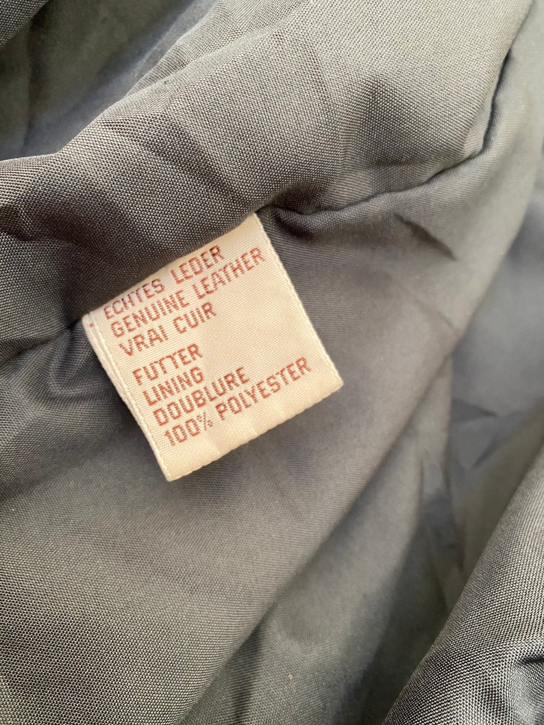 K&ouml;nnte beinhalten: Ein braunes Leder-Etikett mit wei&szlig;em Text, der "Echtes Leder Genuine Leather Vrai Cuir Futter Lining Doublure 100% Polyester" lautet.
