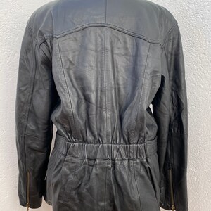 K&ouml;nnte beinhalten: Schwarze Lederjacke mit Kunstfellkragen. Die Jacke hat eine eingezogene Taille und Rei&szlig;verschlusstaschen.