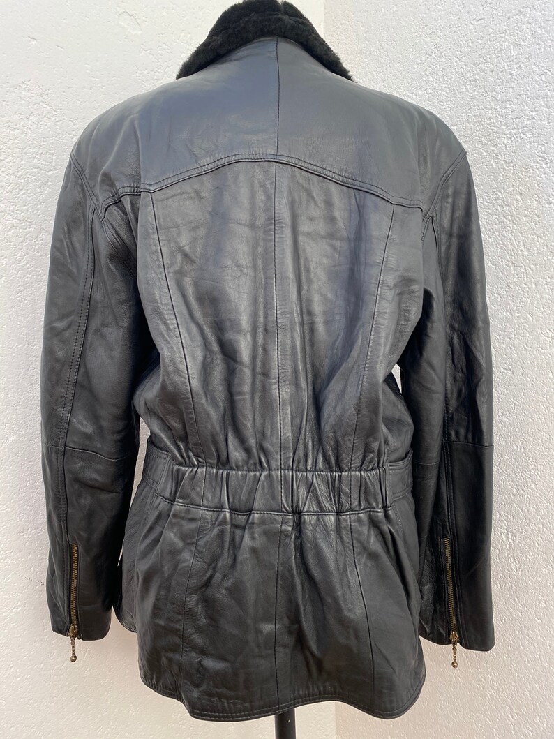 K&ouml;nnte beinhalten: Schwarze Lederjacke mit Kunstfellkragen. Die Jacke hat eine eingezogene Taille und Rei&szlig;verschlusstaschen.