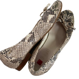 May include: A pair of beige ballet flats with a snake print design. The flats have a bow on the front and the brand name "T.B.S.I" is visible on the insole.