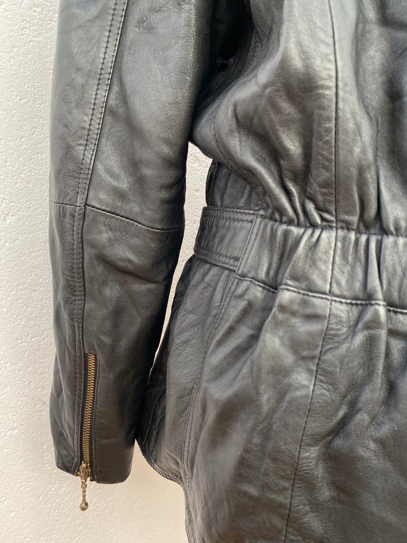 K&ouml;nnte beinhalten: Schwarze Lederjacke mit Rei&szlig;verschlussdetail am &Auml;rmel und einer taillierten Taille.