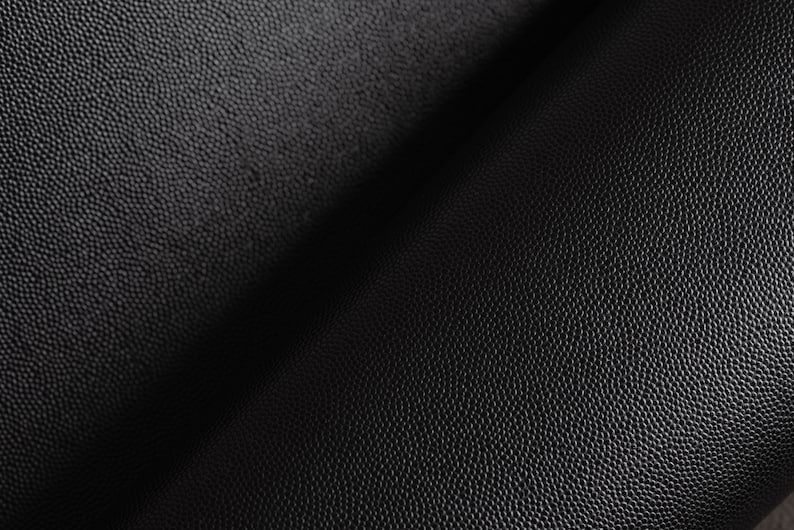 May include: Close-up of black textured leather with a subtle sheen. The leather has a pebbled surface and is folded in half.
