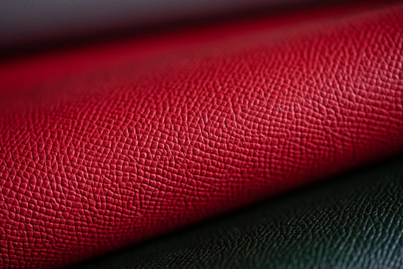 May include: Close-up of red and dark green leather material. The red leather is textured with a fine, repeating pattern. The dark green leather is visible in the lower portion of the image, creating a contrast.