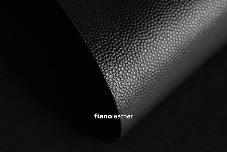 May include: Close-up of black textured leather with a subtle sheen. The leather is folded over, creating a curved shape. The text "fianoleather" is visible in the lower right corner.