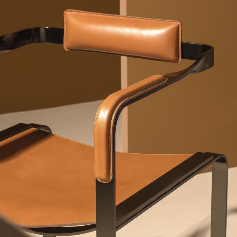 Puede incluir: Una silla de cuero marr&oacute;n con estructura de metal negro. La silla tiene un reposacabezas y reposabrazos acolchados.