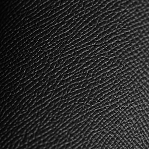 May include: Close-up of black leather with a textured surface. The leather has a pattern of small, irregular shapes and lines, creating a detailed and tactile appearance. The lighting highlights the texture, giving it depth and dimension.