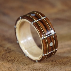 May include: A wooden ring with a brown and gold striped pattern and white accents. The ring is made of wood and has a polished finish.