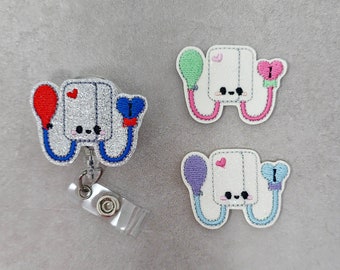 May include: Three embroidered badge reel clips with a cartoon blood pressure cuff design. Each clip has a different colored balloon attached to the cuff. The balloons are red, green, and purple.