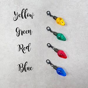 May include: Four light bulb charms in yellow, green, red, and blue. Each charm has a black metal loop for attaching to a zipper pull or other item.