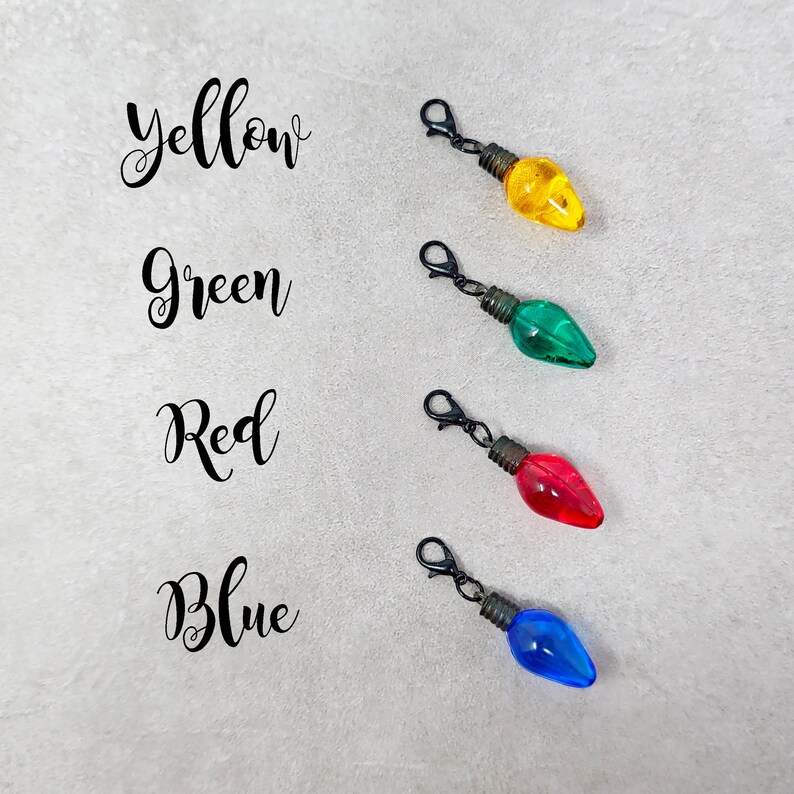 May include: Four light bulb charms in yellow, green, red, and blue. Each charm has a black metal loop for attaching to a zipper pull or other item.