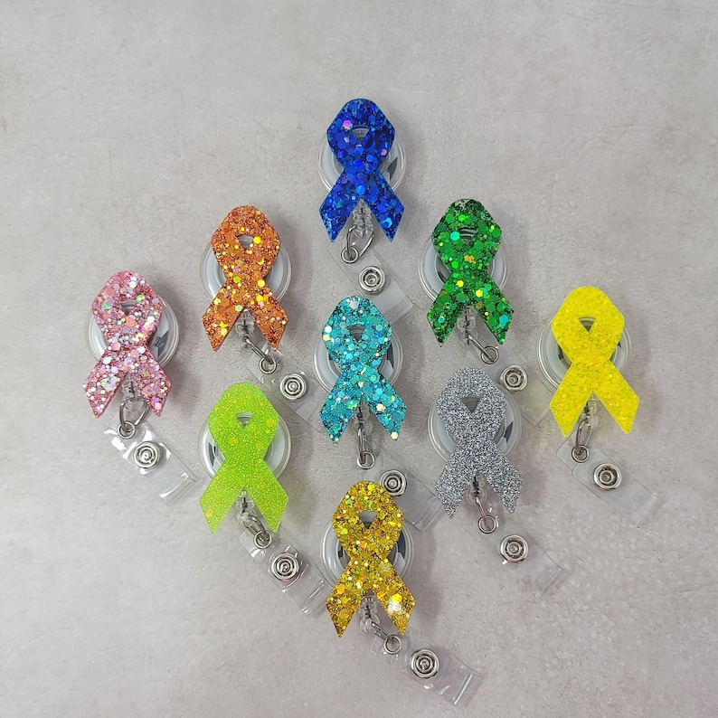 Op de afbeelding: Assortiment van tien kleurrijke glitterlint-badge-rollen. Elke rol heeft een ander gekleurd lint met een glitterafwerking. De linten zijn bevestigd aan een zilveren metalen badge-rol.