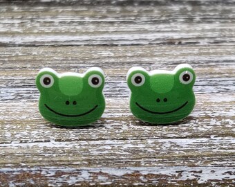 May include: A pair of green frog-shaped earrings with white eyes and a white outline. The earrings are made of polymer clay and have a glossy finish.
