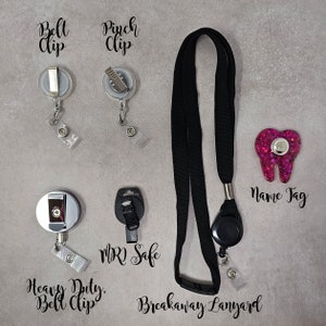 Op de afbeelding: Een zwarte afneembare lanyard met een intrekbare badgehouder. De lanyard heeft een zilveren clip en een roze glittertand naamplaatje. De afbeelding toont ook verschillende soorten badgeclips, waaronder een zware riemclip, een knijpclip en een MRI-veilige clip.