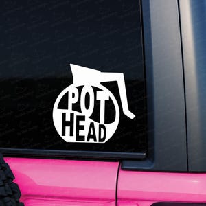 May include: A white vinyl decal applied to a dark window, featuring the silhouette of a coffee pot with the text POT HEAD integrated into the design. The graphic is composed of bold, clean lines forming the shape of a carafe and handle.