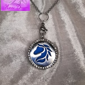 Könnte beinhalten: Silberfarbene Halskette mit einem runden Anhänger mit einem blauen Pferdekopf-Design. Der Anhänger ist mit kleinen, klaren Kristallen besetzt. Die Halskette hat eine Kette und einen Verschluss. Das Bild enthält auch ein Logo mit der Aufschrift "Horse Dreams".