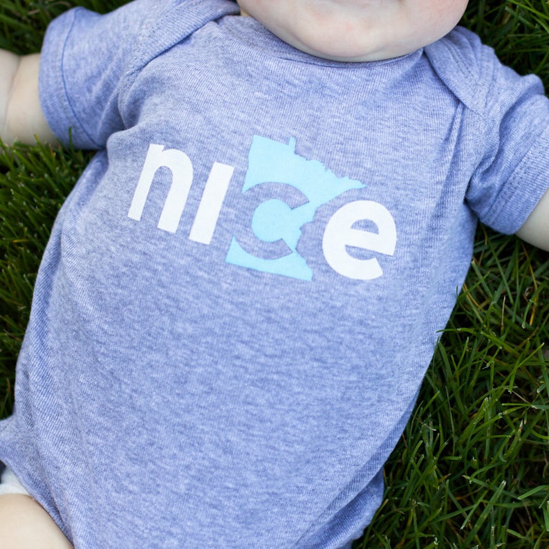 Puede incluir: Un body de beb&eacute; azul claro con la palabra "nice" impresa en letras blancas, con la letra "c" reemplazada por el contorno del estado de Minnesota en azul claro.