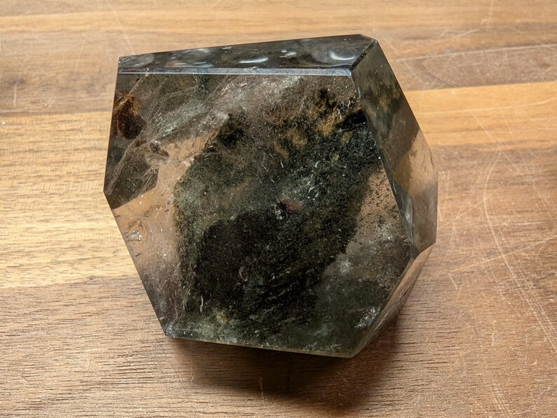 May include: A large, clear, faceted crystal with dark green inclusions. The crystal is shaped like a hexagon and has a smooth, polished surface.