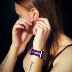 May include: A woman's wrist with a tattoo that reads "Heart is all you need except for a good pair of shoes" and a black and pink striped watch band.