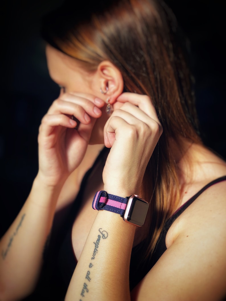May include: A woman's wrist with a tattoo that reads "Heart is all you need except for a good pair of shoes" and a black and pink striped watch band.
