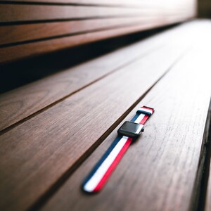 May include: A red, white, and blue striped watch band on a wooden surface.