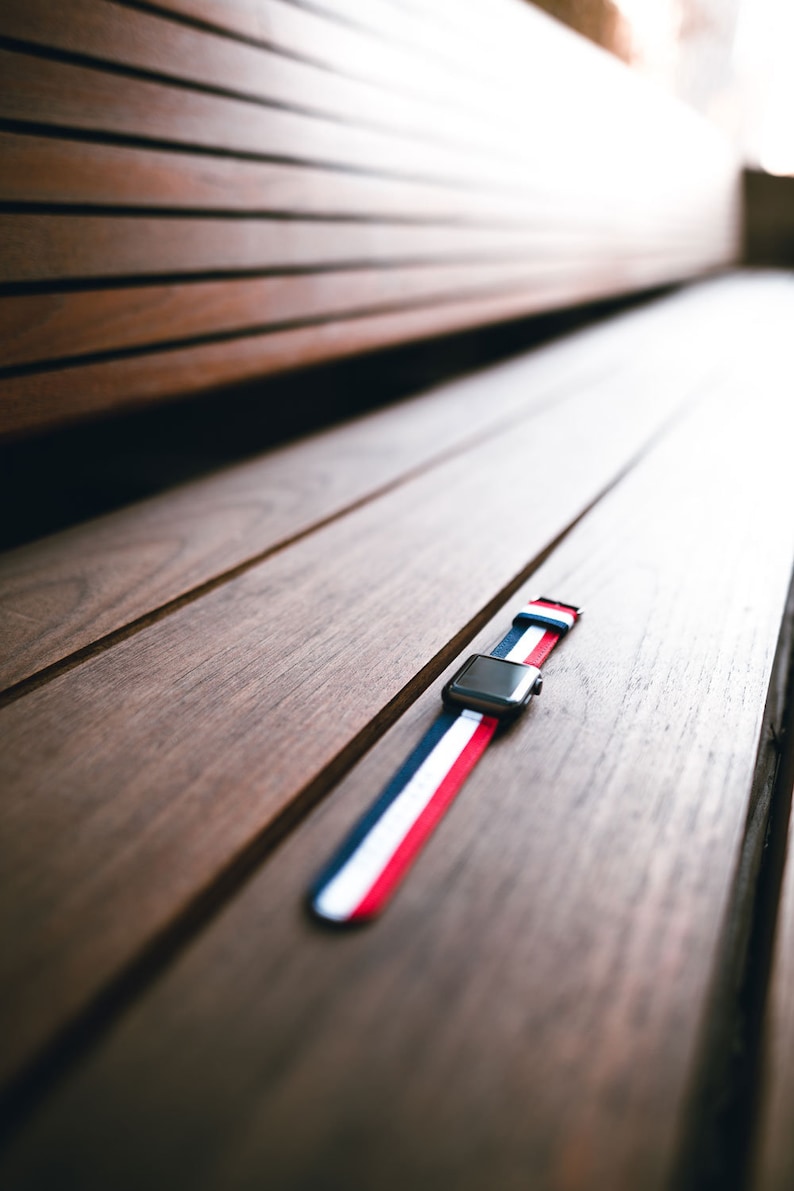 May include: A red, white, and blue striped watch band on a wooden surface.