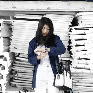 May include: A woman wearing a blue denim jacket, white pants, and a black and white handbag. She is checking the time on a smartwatch on her left wrist.