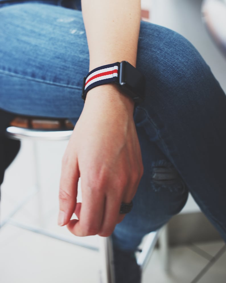 May include: A person wearing blue jeans with a watch with a red, white, and blue striped band.