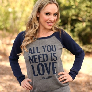 May include: A grey and navy blue raglan sweatshirt with the text "All you need is love... and coffee" printed on the front.