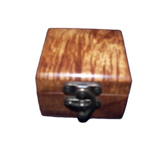 May include: A small, square wooden box with a hinged lid and a dark metal clasp. The box has a warm, brown color with a natural wood grain pattern. The clasp is a dark, antique metal. The box is likely used for jewelry or small keepsakes.