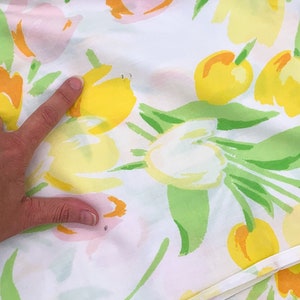 May include: White fabric with a floral print featuring yellow, pink, and green tulips. The fabric has a smooth texture and a subtle sheen.
