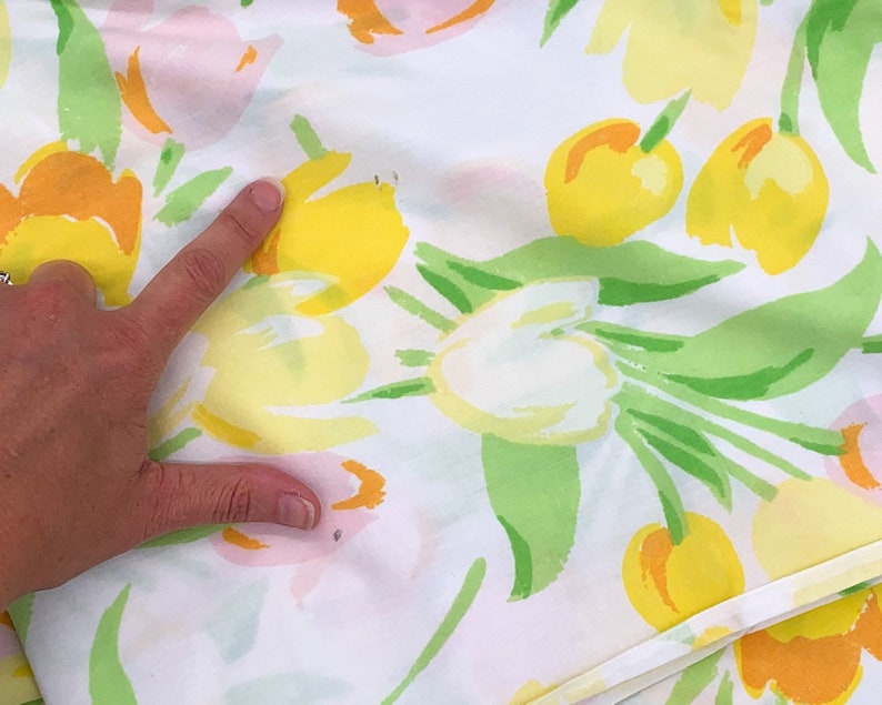 May include: White fabric with a floral print featuring yellow, pink, and green tulips. The fabric has a smooth texture and a subtle sheen.