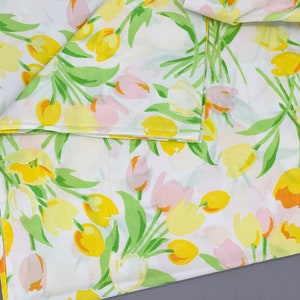 May include: White fabric with a repeating pattern of yellow and pink tulips with green stems and leaves.