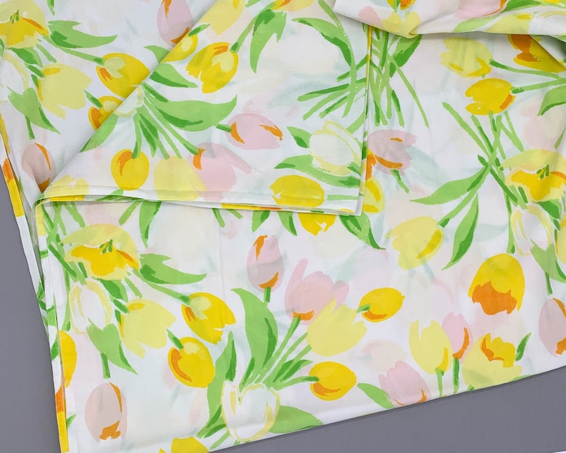 May include: White fabric with a repeating pattern of yellow and pink tulips with green stems and leaves.