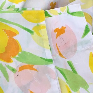 May include: White fabric with a floral print of yellow, orange, and pink tulips. The fabric has a green stem and leaf design.