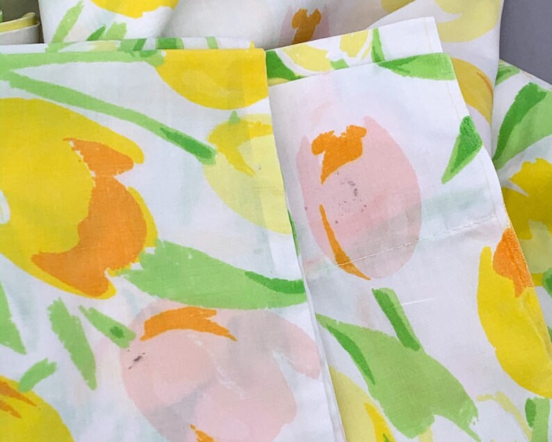 May include: White fabric with a floral print of yellow, orange, and pink tulips. The fabric has a green stem and leaf design.
