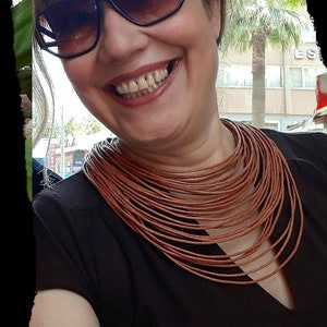 May include: A woman wearing sunglasses and a black top with a brown leather necklace. She is smiling and looking at the camera.
