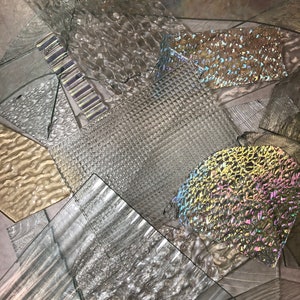 May include: Assortment of clear glass sheets with various textures, including wavy, ribbed, and patterned. The glass sheets are arranged in a random pattern.