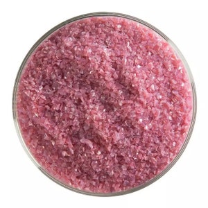 May include: A close-up view of a bowl filled with pink and iridescent glass glitter. The glitter is small and has a shimmery finish.