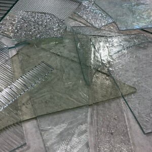 May include: A collection of clear glass sheets with various textures, including ribbed, textured, and smooth. The glass sheets are arranged in a random pattern.