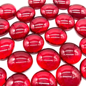 May include: A collection of red glass pebbles, smooth and shiny, with a slight oval shape.