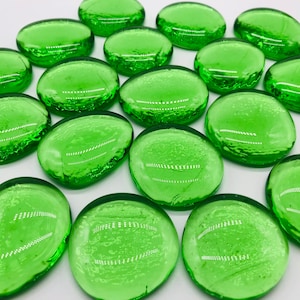 May include: A collection of smooth, green glass stones. The stones are oval shaped and have a slightly textured surface.